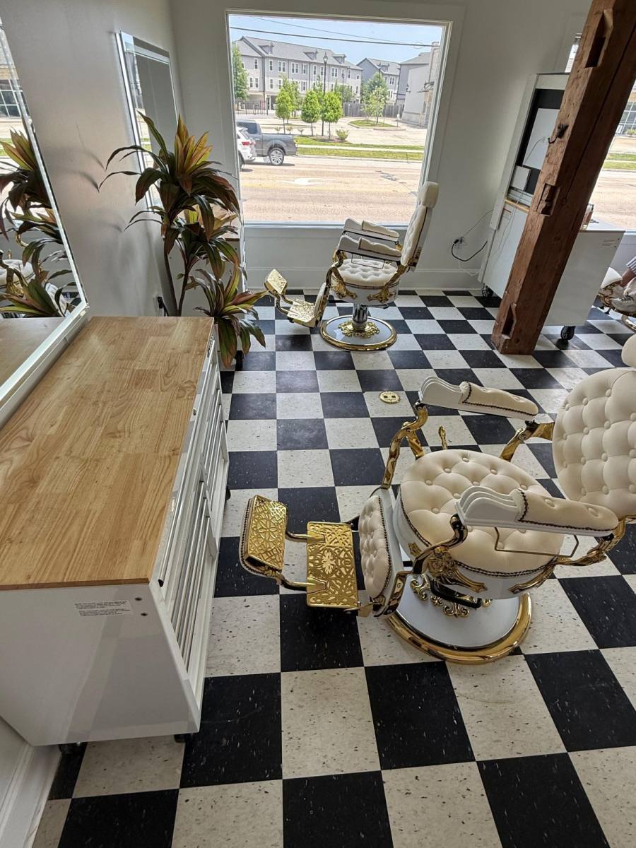 The shop's interior: black-and-white checkerboard floor, white-and-gold vintage barber chairs, exposed wood beam.