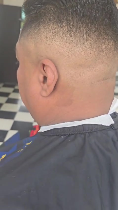 The back of a client's head showing a crisp skin fade and a sharp line-up against the shop's checkerboard floor.