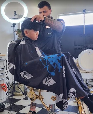 Adahias mid-cut, working on a young client under the shop's ring light.